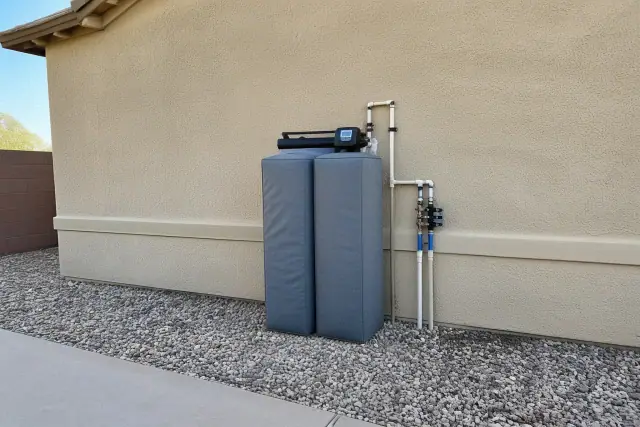 Water softener with an insulated cover and neat plumbing installed against an exterior wall in Mesa, AZ.