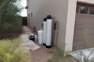 Water softener system with white resin tanks and copper pipes installed next to a garage in Mesa, AZ.
