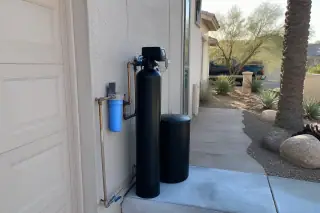 Saltless water softener with clean piping mounted on a stucco wall near a garage and xeriscaped yard in Mesa, AZ.