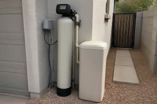 Reset water softener unit with new plumbing pipes next to a garage in Mesa, AZ.