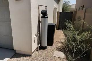 Water softener unit with neatly routed plumbing installed against a stucco wall at a home in Mesa, AZ.