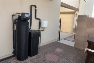 Water softener unit with insulated plumbing pipes against a stucco wall at a home in Mesa, AZ.