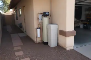 Water softener system with new plumbing pipes installed against a stucco wall at a home in Mesa, AZ.