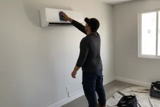 Technician wiping down a ductless AC unit on a finished wall in a Phoenix, AZ home.