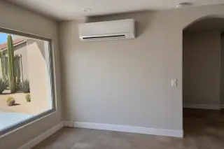 Ductless AC unit mounted on a finished wall with desert landscaping visible through a window in Phoenix, AZ.