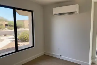 Ductless heat pump indoor unit mounted on a finished wall with refrigerant lines near the baseboard in Phoenix, AZ.