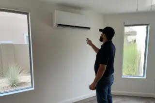 Technician inspecting a wall-mounted mini split unit in a Phoenix, AZ garage with xeriscaping visible through the window.