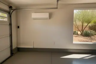 Wall-mounted ductless mini split in a garage with desert landscaping visible through the window in Phoenix, AZ.