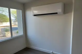 Indoor mini split unit on a wall with refrigerant lines by a window showing xeriscaping in Phoenix, AZ.