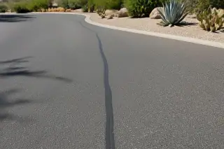 Cured rubberized sealant flush in a paved parking lot crack with agave plants nearby in Peoria, AZ.