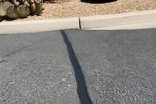Rubberized sealant filling a crack in a weathered asphalt parking lot with prickly pear cacti in Peoria, AZ.