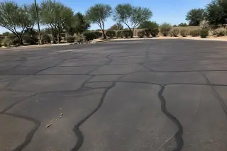 Dark linear sealant ribbons filling cracks on a finished asphalt parking lot in Peoria, AZ.