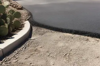 Close-up of a new asphalt seam overlapping old pavement next to prickly pear cacti in Peoria, AZ.