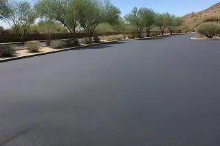 Freshly compacted asphalt surface next to creosote bushes under bright sunlight in Peoria, AZ.
