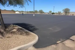A worker inspects a smooth, unpainted asphalt parking lot with desert gravel landscaping in Peoria, AZ.