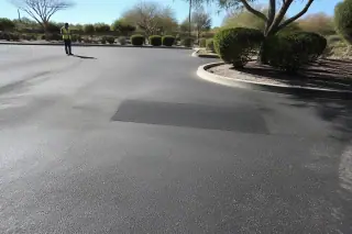 Compact asphalt patch on a finished parking lot surface with desert shrubs in the background in Peoria, AZ.