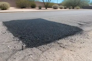 Compacted asphalt patch surrounded by desert sagebrush and palo verde trees in a Peoria, AZ parking lot.