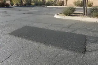 Patched pothole with textured asphalt seams in a parking lot with desert gravel landscaping in Peoria, AZ.