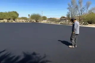 Worker inspecting a smooth, unpainted asphalt parking lot with prickly pear cacti in Peoria, AZ.