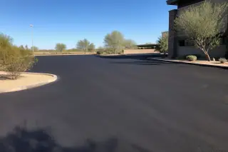 Wide view of a freshly sealcoated asphalt parking lot with desert scrub in Peoria, AZ.