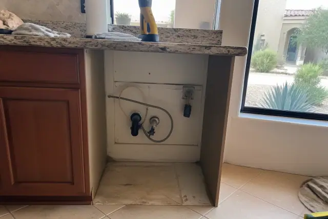 Empty dishwasher cavity with plumbing and wiring under a kitchen counter in a Phoenix, AZ home.