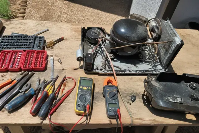 Refrigerator internal cooling components undergoing diagnostics with a multimeter on a workbench in Phoenix, AZ.