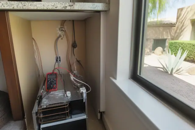 Technician repairing a built-in ice maker with copper water lines and a multimeter in a Phoenix, AZ kitchen.