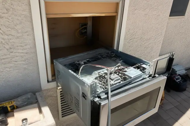 Built-in microwave undergoing repair with exposed wiring in a cabinet cutout at a job site in Phoenix, AZ.
