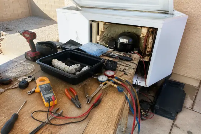 Technician repairing a chest freezer with tools and testing equipment on a workbench in Phoenix, AZ.