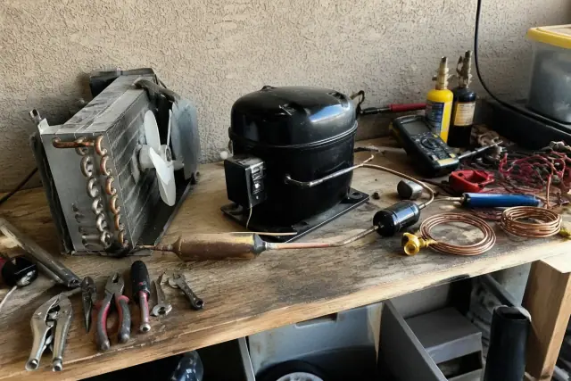 Refrigerator compressor and sealed-system components being repaired on a workshop workbench in Phoenix, AZ.