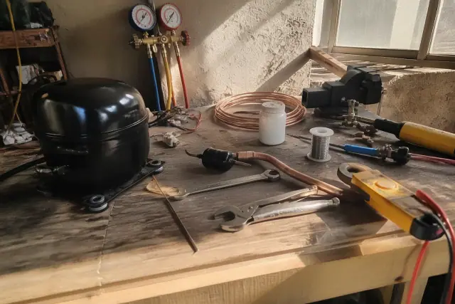 Technician repairing a freezer compressor on a workbench in Phoenix, AZ, with tools and copper tubing.