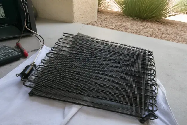 Technician cleaning a refrigerator condenser coil assembly on a cloth floor mat in Phoenix, AZ.