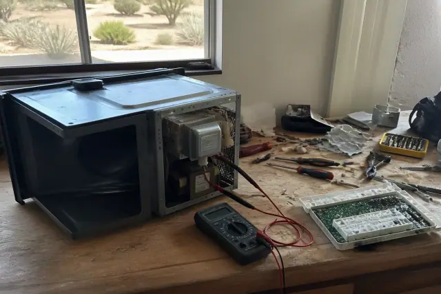 A technician servicing countertop microwaves on a wooden workbench in a Phoenix, AZ workshop.