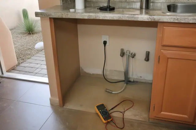 Empty kitchen cabinet space for dishwasher repair with electrical wiring and plumbing in a Peoria, AZ home.