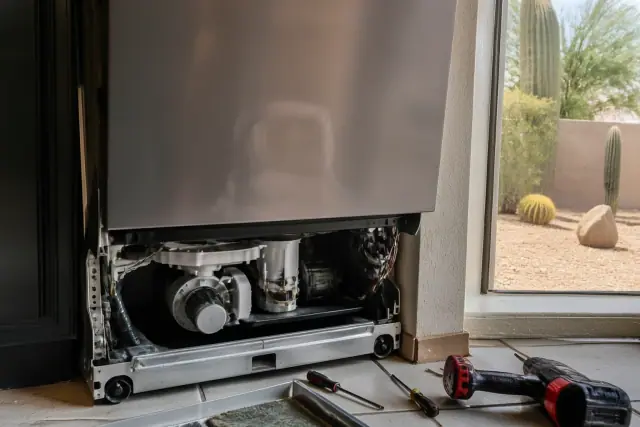 Technician repairing a dishwasher with exposed internal components in a kitchen in Gilbert, AZ.