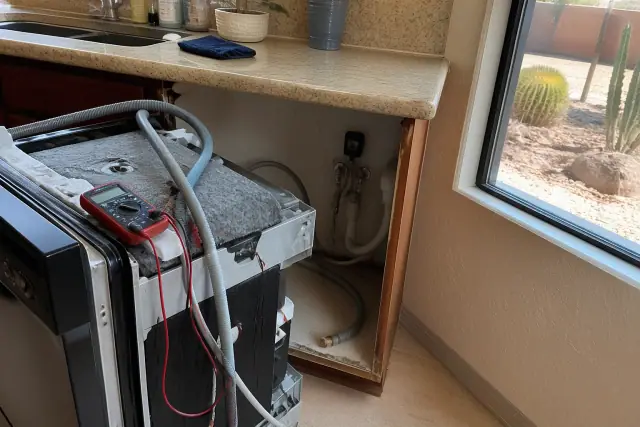 A dishwasher pulled out for repairs with hoses and a multimeter in a kitchen in Glendale, AZ.