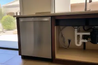 A clean, installed dishwasher with visible plumbing and wiring under a kitchen counter in a Phoenix, AZ home.