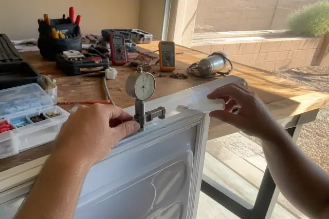 Technician repairing a freezer door gasket with a tension gauge in a Phoenix, AZ workshop.