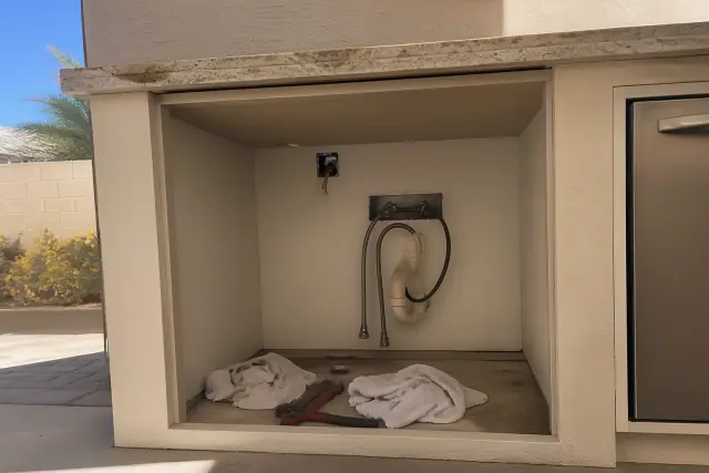 Plumbing tools and cloths inside an under-counter cavity during a freezer leak repair in Phoenix, AZ.