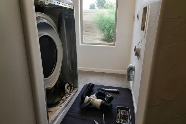 Technician repairing a washer drain pump and hoses on a work mat in a Phoenix, AZ laundry closet.