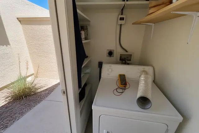 A technician repairing a dryer in a laundry closet with a multimeter on top in Phoenix, AZ.