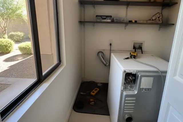Technician repairing a dryer in a laundry closet in Mesa, AZ, showing disconnected venting and diagnostic tools.