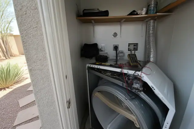 A dryer pulled out for repairs in a laundry closet in Phoenix, AZ, with diagnostic tools and vents visible.