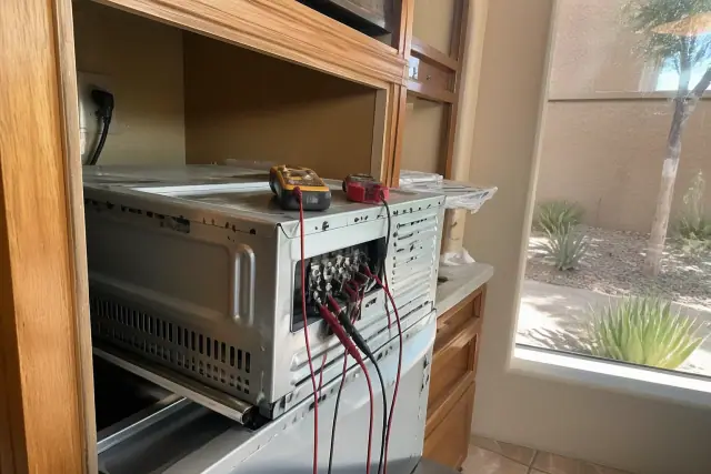 A technician repairing an electric oven with exposed wiring and a multimeter in a Phoenix, AZ kitchen.