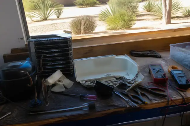 Freezer repair in progress on a workbench in Tempe, AZ, with desert landscaping visible through the window.