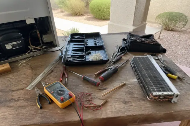 A workshop workbench in Mesa, AZ with tools, a multimeter, and disassembled freezer parts for repair.