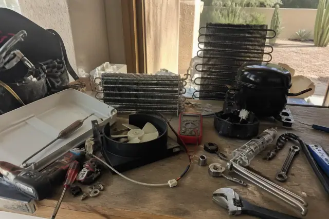 Disassembled freezer parts and repair tools on a wooden workbench at a workshop in Scottsdale, AZ.