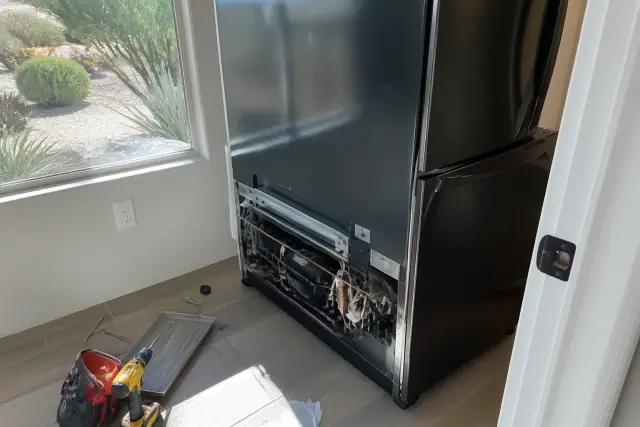French door refrigerator undergoing repair in a Phoenix, AZ pantry with exposed wiring and desert landscaping outside.