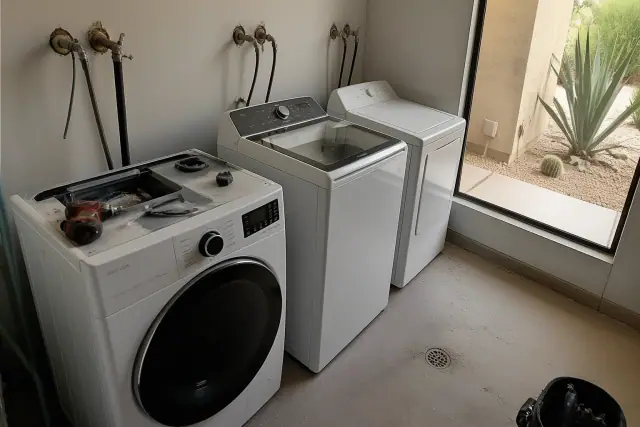 Utility room in Phoenix, AZ featuring wall-mounted water valves, a floor drain, and various laundry machines.