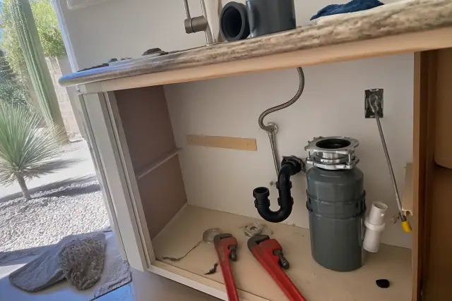 Technician repairing a garbage disposal under a kitchen sink in a Mesa, AZ home with plumbing tools visible.